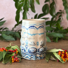 Load image into Gallery viewer, A handmade ceramic vase with undulating textures featuring a blue swirl patterns, styled on a wooden surface with green leaves and small orange flowers.