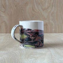 Load image into Gallery viewer, Marbled black, red, and gold ceramic mug on a wooden surface with a wooden background