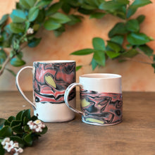 Load image into Gallery viewer, Two ceramic mugs with artistic designs on a wooden surface with greenery in the background