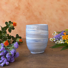 Load image into Gallery viewer, Blue and gray ceramic cup on a wooden surface with flowers on a Sienna background