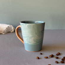 Load image into Gallery viewer, Blue ceramic mug on a gray surface with scattered coffee beans