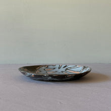 Load image into Gallery viewer, Black ceramic plate with abstract design on a gray surface and background