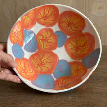 Load image into Gallery viewer, A hand holds a white ceramic bowl decorated with organic orange and yellow patterns and blue and purple egg shapes, set against a wooden background.
