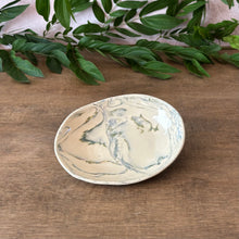 Load image into Gallery viewer, An oval ceramic dish with a marbled cream and green pattern, styled on a wooden tabletop with green leaves in the background.

