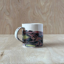 Load image into Gallery viewer, Marbled black, red, and gold ceramic mug on a wooden surface with a wooden background
