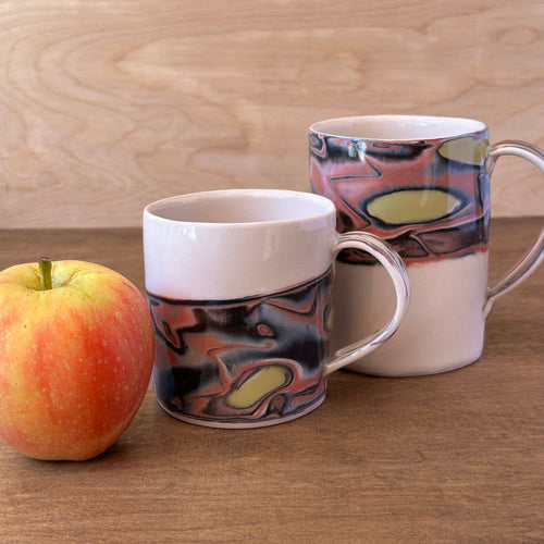 Two ceramic mugs with marbled design next to an apple on a wooden surface