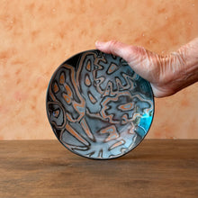 Load image into Gallery viewer, Hand holding a shallow ceramic bowl with a unique pattern against a wooden surface
