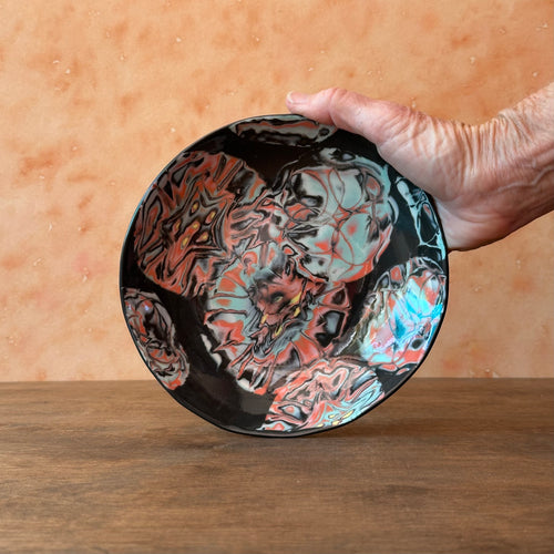 Hand holding a marbled ceramic plate with a colorful design on a wooden surface.