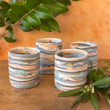 Load image into Gallery viewer, Set of four striped ceramic tumblers on a wooden surface with green leaves.

