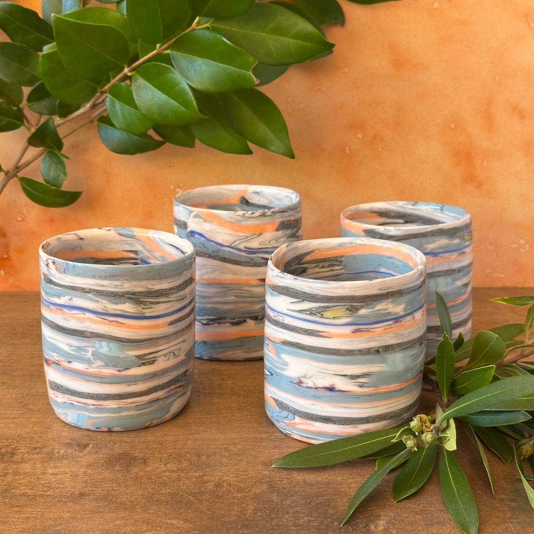 Set of four striped ceramic tumblers on a wooden surface with green leaves.