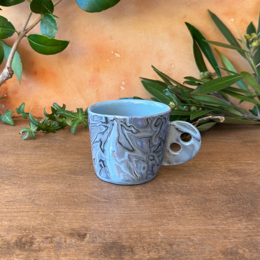 Blue ceramic espresso cup with decorative patterns on a wooden surface with green leaves in the background