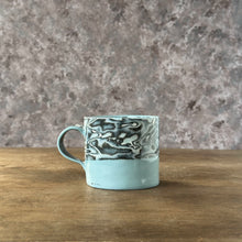 Load image into Gallery viewer, Ceramic mug with textured design on a wooden surface and stone wall background
