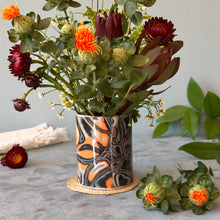 Load image into Gallery viewer, Bouquet of flowers in a decorative vase on a gray surface with additional flowers and leaves.
