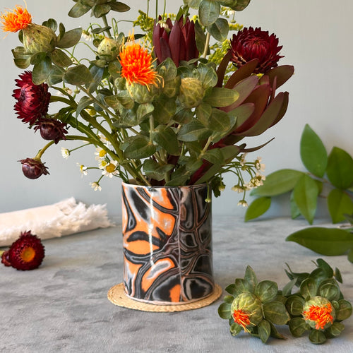 Bouquet of flowers in a decorative vase on a gray surface with additional flowers and leaves.