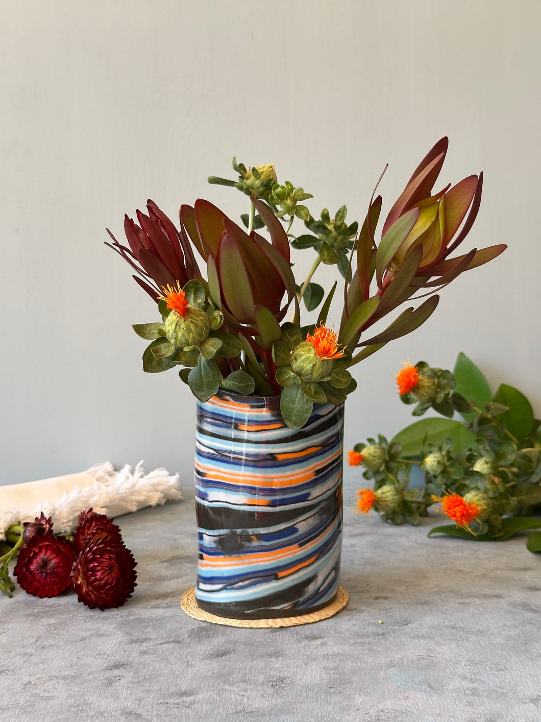 Decorative vase with striped pattern filled with greenery and flowers on a neutral background