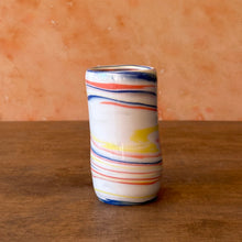 Load image into Gallery viewer, Cylindrical porcelain vase with multicolored stripes on a wooden surface and terracotta wall background

