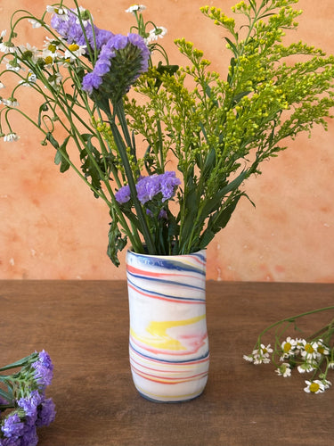 Striped red, blue, and yellow porcelain vase with flowers on a wooden surface