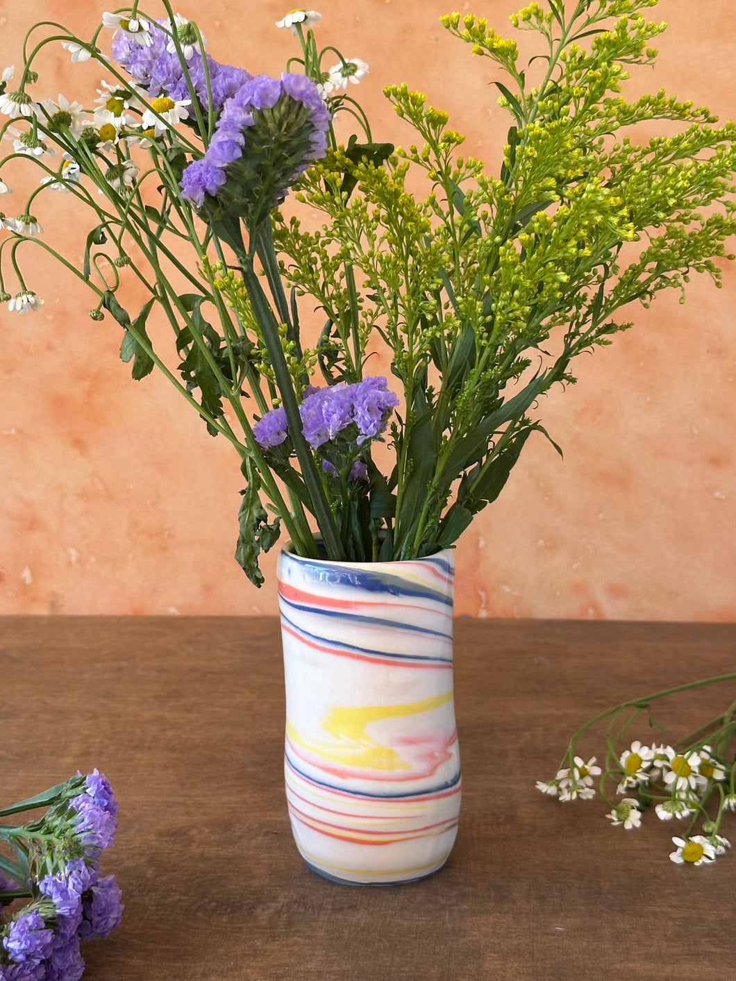 Striped red, blue, and yellow porcelain vase with flowers on a wooden surface