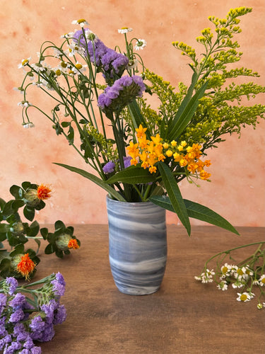Bouquet of flowers in a gray and white vase on a wooden surface 