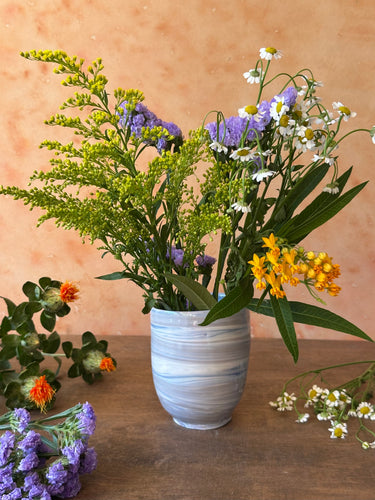 Vase with blue and gray marbled pattern with flowers on a wooden surface against a beige background