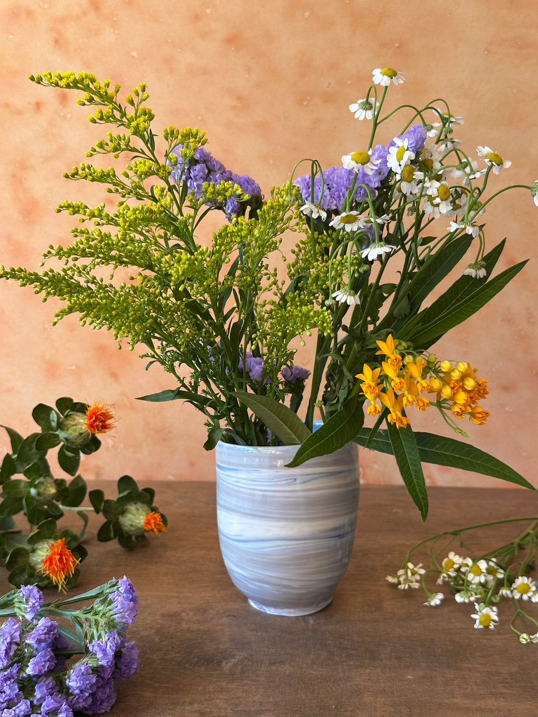 Vase with blue and gray marbled pattern with flowers on a wooden surface against a beige background
