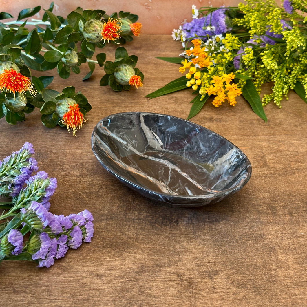 Black marbled ceramic dish on a wooden surface with flowers around it