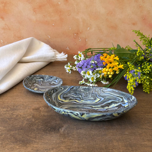 Marbled ceramic bowl and smaller dish on a wooden surface with flowers and a cloth.