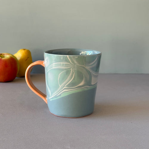 Blue ceramic mug with a water pattern on a gray surface with apples in the background