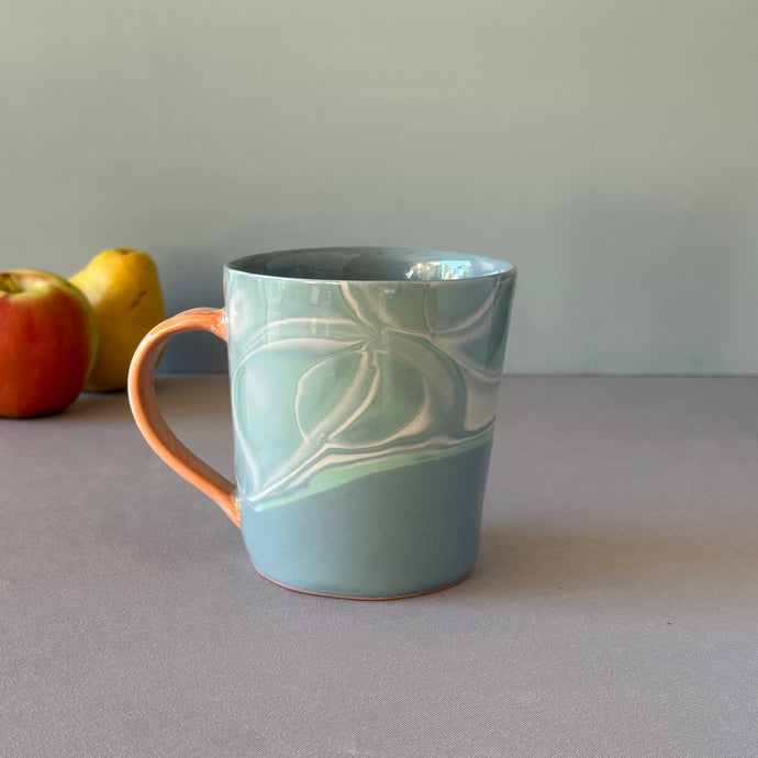Blue ceramic mug with a water pattern on a gray surface with apples in the background