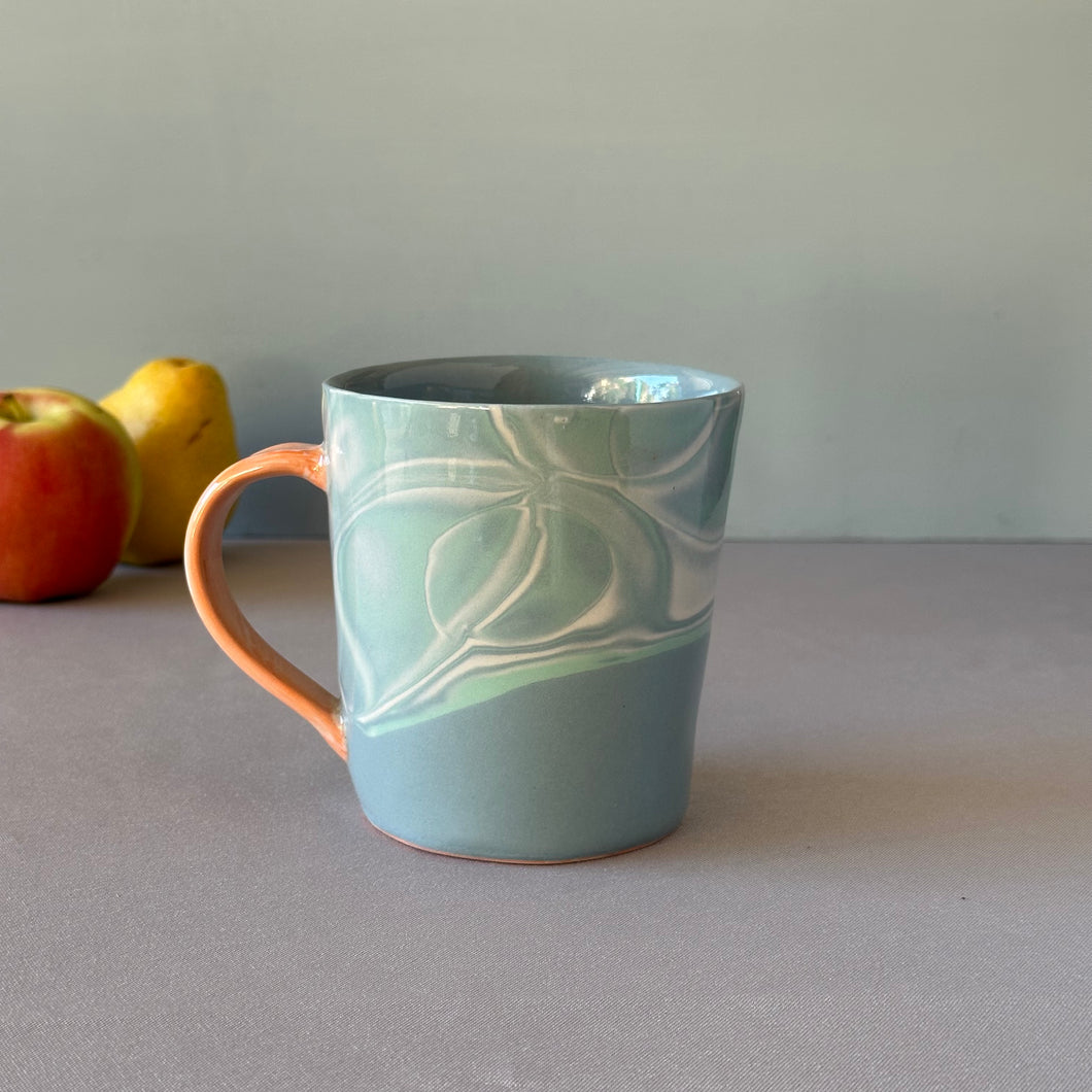 Blue ceramic mug with a water pattern on a gray surface with apples in the background