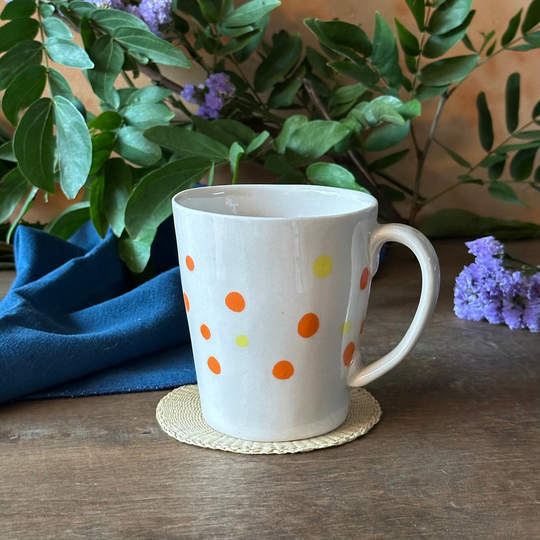 White mug with colorful polka dots on a wooden surface with plants in the background