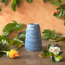 Load image into Gallery viewer, Blue textured vase on a wooden surface with green leaves and flowers in the background

