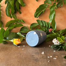 Load image into Gallery viewer, Bottom view of blue cylindrical vase with floral and leaf decorations on a wooden surface
